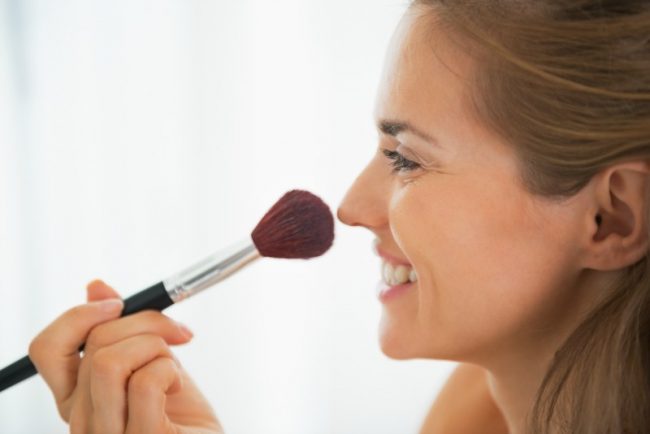 Happy young woman using makeup brush