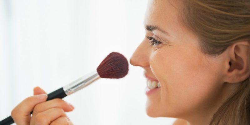 Happy young woman using makeup brush
