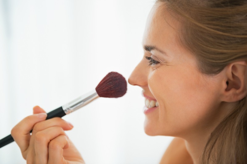 Happy young woman using makeup brush